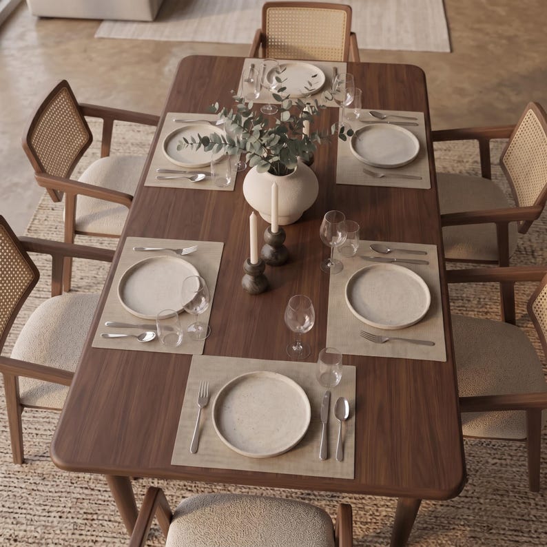 May include: A rectangular dark wood dining table set for six with light-colored placemats, white ceramic plates, stainless steel silverware, clear glassware, two dark gray candle holders with white taper candles, and a central white vase.
