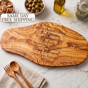 May include: A wooden cutting board with a natural wood grain pattern. The board has engraved text that reads "Never underestimate the difference you have made and the lives you have touched. Happy Retirement." Includes a wooden fork and spoon.