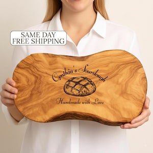 May include: A wooden breadboard with a natural wood grain finish. The board features the text "Cynthia's Sourdough" and "Handmade with Love" along with an illustration of a loaf of bread.