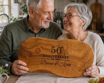 May include: An oval-shaped wooden serving board with natural grain patterns, engraved with the text 50th ANNIVERSARY est. 1986 Danna & Kevin. The board features a smooth, light brown finish and irregular, organic edges, showcasing the wood's texture.