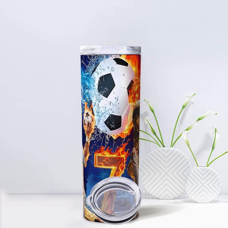 Peut inclure: Un gobelet en acier inoxydable avec un motif de ballon de football, des flammes et des &eacute;l&eacute;ments aquatiques. Le chiffre 7 est affich&eacute;. Le gobelet a un couvercle transparent et est d&eacute;cor&eacute; d'un graphisme dynamique et vibrant.