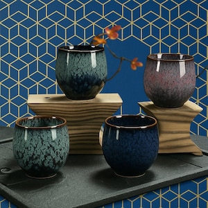 Puede incluir: Cuatro tazas de té de cerámica con un esmalte moteado en tonos de azul, verde y rosa. Las tazas están dispuestas en una plataforma de madera.