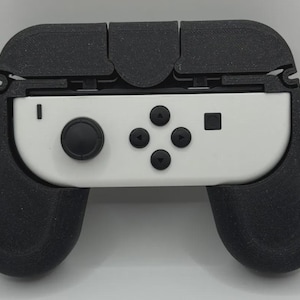 May include: A white video game controller component featuring a black circular joystick, four directional buttons, and a square button, securely fitted into a textured black plastic ergonomic grip frame that extends around the sides and top.