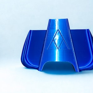 May include: A glossy, royal blue 3D-printed plastic component featuring a central raised triangular emblem composed of three smaller triangles. The object has a symmetrical, curved, and flared design with a smooth, reflective surface finish.