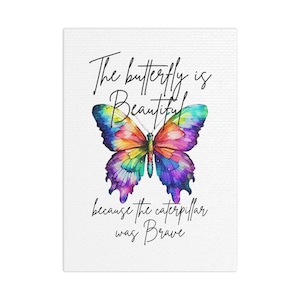 May include: A canvas print with a colourful watercolour butterfly design. The butterfly is depicted in shades of blue, purple, yellow, and orange. The text reads "The butterfly is Beautiful because the caterpillar was Brave" in black script.