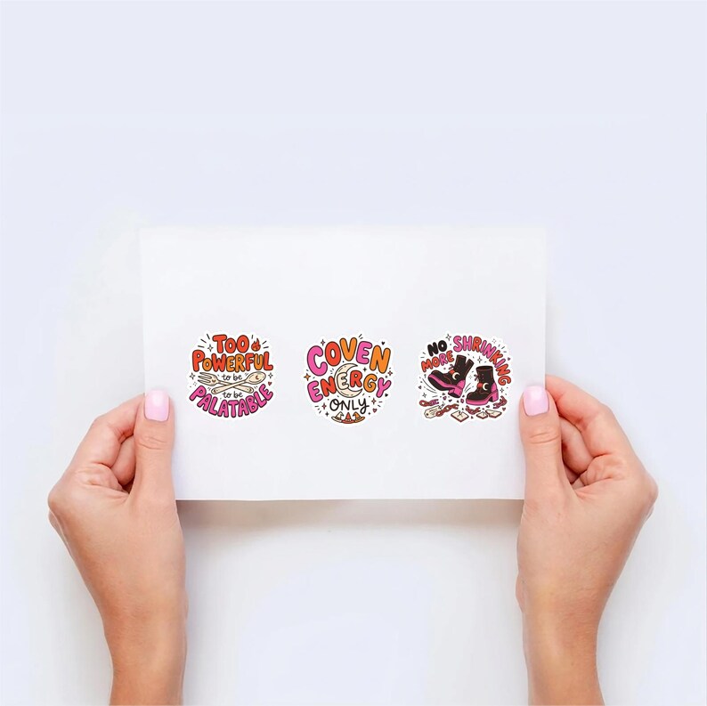 Op de afbeelding: Drie ronde stickers op een wit vel. De eerste bevat de tekst 'TOO POWERFUL TO BE PALATABLE' met een vork en lepel. De tweede zegt 'COVEN ENERGY ONLY' met een maansikkel. De derde toont 'NO MORE SHRINKING' met twee zwarte laarzen.