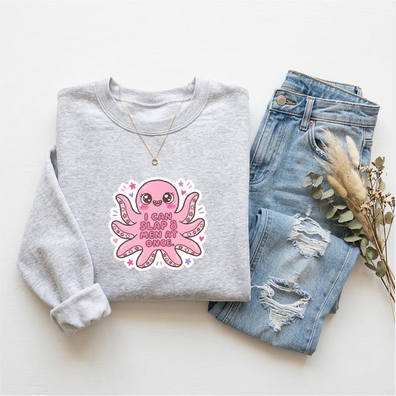 Pode incluir: Um moletom cinza claro com um gr&aacute;fico de polvo rosa que diz "I CAN SLAP 8 MEN AT ONCE." O moletom &eacute; combinado com jeans rasgados azul claro e um colar de ouro. Um raminho de flores secas tamb&eacute;m est&aacute; presente.