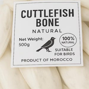 Puede incluir: Una bolsa de plástico transparente llena de huesos de sepia blanquecinos. Una etiqueta dice "CUTTLEFISH BONE NATURAL" con una ilustración de un pájaro y "SUITABLE FOR BIRDS". El peso neto es de 500g. La bolsa tiene un cierre verde.