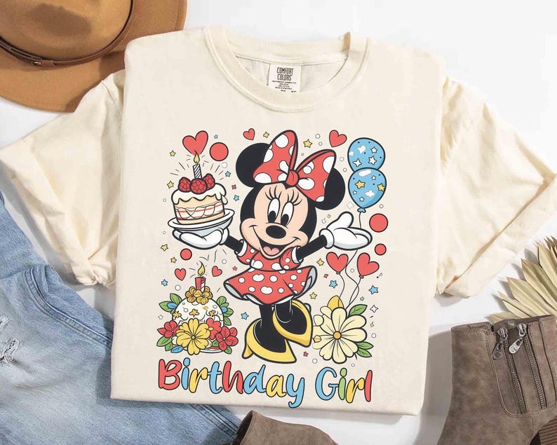Peut inclure: T-shirt cr&egrave;me avec un motif Minnie Mouse color&eacute;. Minnie tient un g&acirc;teau et des ballons, avec les mots "Birthday Girl" en dessous. Le motif comprend des c&oelig;urs, des fleurs et un g&acirc;teau d'anniversaire.