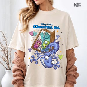Puede incluir: Camiseta color marfil con el logotipo de Disney Pixar Monsters, Inc. y personajes. El diseño incluye a Sully, Mike Wazowski, Boo y un monstruo morado. Globos y estrellas completan el diseño juguetón.