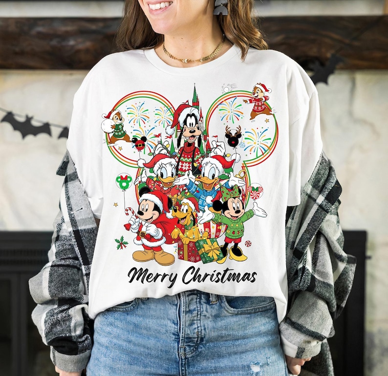 May include: White t-shirt featuring a festive Disney Christmas design. The graphic includes Mickey Mouse, Minnie Mouse, Donald Duck, and other characters in Santa hats, with the text "Merry Christmas" in a script font.