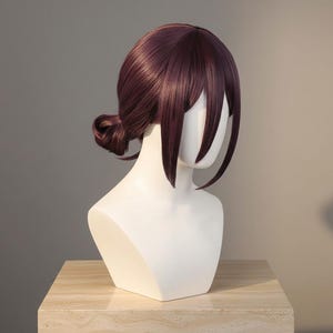 May include: A dark burgundy wig, featuring a low bun and long, face-framing bangs. The wig is displayed on a white mannequin head, highlighting the colour and style. The hair has a smooth texture, suitable for cosplay or costume use.