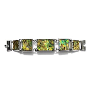 Puede incluir: Un brazalete plateado con segmentos rectangulares con incrustaciones de concha de abulón iridiscente verde y amarillo. El brazalete tiene un cierre y se muestra sobre un fondo blanco. La pieza de joyería es un accesorio de moda.
