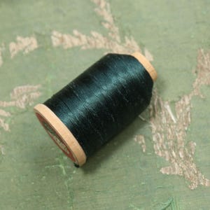 May include: A spool of dark green thread wound around a wooden bobbin.