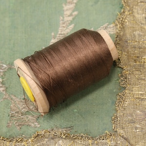 May include: A spool of brown thread wound around a wooden bobbin with a yellow plastic cap.