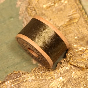 May include: A spool of dark green thread wound around a wooden bobbin. The bobbin has a label with text that is difficult to read.