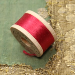 May include: A wooden spool of red thread with a white stripe.