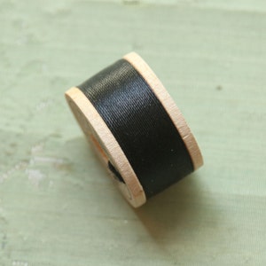 May include: A spool of black thread wound around a wooden bobbin.