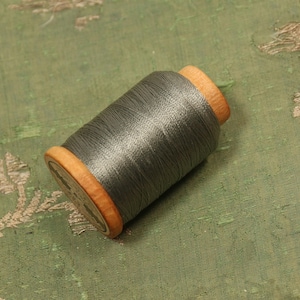 May include: A spool of gray thread wound around a wooden bobbin. The thread is smooth and shiny.