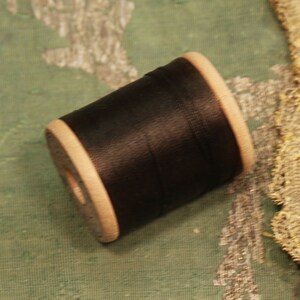 May include: A spool of black thread with a wooden bobbin.