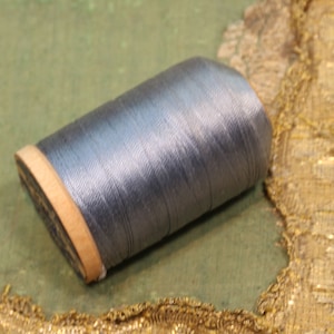 May include: A spool of silver gray thread with a wooden bobbin.