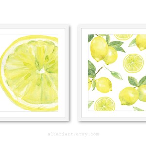 Peut inclure: Deux impressions encadrées à l'aquarelle de citrons. L'une montre une tranche de citron, l'autre affiche des citrons entiers et des tranches avec des feuilles vertes sur fond blanc. Les impressions sont dans des cadres blancs.