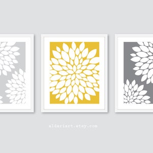 May include: Three framed floral art prints. Each print features a white floral design against a gray or yellow background. The frames are white. The website address aldariart.etsy.com is at the bottom.