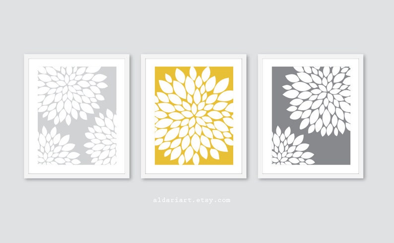 May include: Three framed floral art prints. Each print features a white floral design against a gray or yellow background. The frames are white. The website address aldariart.etsy.com is at the bottom.