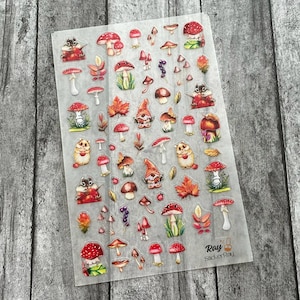 May include: A clear sticker sheet featuring various whimsical illustrations. The designs include red and white mushrooms, autumn leaves, gnomes, and small woodland creatures. The sheet has the text "Ray StickerRay" printed in the bottom right corner.