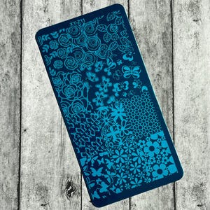 May include: A rectangular nail art stamping plate in dark blue with various floral and butterfly designs in a lighter blue. The plate includes roses, butterflies, and other floral patterns. The text "XY-211" is visible.