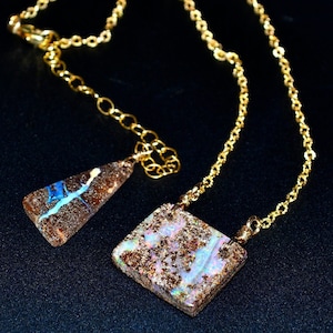 May include: Two gold necklaces with opal pendants. One pendant is a triangle shape with blue and white streaks. The other pendant is a square shape with pink, white, and blue streaks.