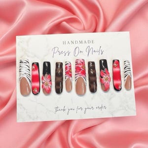 May include: A set of handmade press-on nails with various designs. The nails feature a mix of patterns, including zebra stripes, floral accents, and animal prints. The color palette includes red, black, brown, and nude tones. The card reads "Thank you for your order."