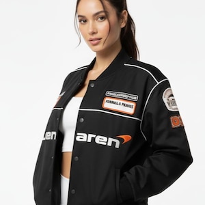 Könnte beinhalten: Schwarze Bomberjacke mit weißem Besatz und mehreren Aufnähern. Die Jacke zeigt das McLaren-Logo und den Text "Formula Prames". Sie hat eine Knopfleiste und zwei Taschen.