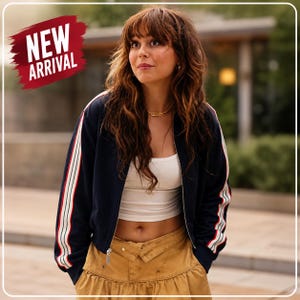 May include: A navy blue bomber jacket with white and red stripes on the sleeves. The jacket is worn over a white crop top and paired with a mustard-colored skirt. The words "NEW ARRIVAL" are displayed in a red banner.