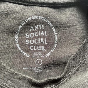 Puede incluir: Primer plano del cuello de una camiseta negra con el texto "ANTI SOCIAL SOCIAL CLUB" en blanco. El texto "EVERYONE GOES AWAY IN THE END" est&aacute; impreso en c&iacute;rculo alrededor del texto principal. La camiseta es talla L y est&aacute; hecha en Honduras.