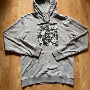 May include: A gray hoodie with a drawstring hood and a kangaroo pocket. The front features a black and white graphic with a logo. The hoodie has ribbed cuffs and hem.