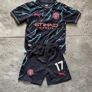 May include: Black soccer jersey and shorts set. The jersey has a round neck and features the "Etihad Airways" logo in orange, with a team emblem and lightning bolt design in light blue and pink. The shorts have the number 17.