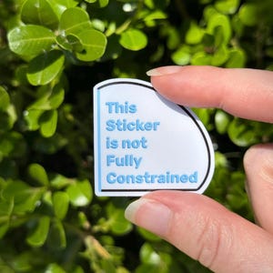 May include: A white sticker with a light blue border and text that reads "This Sticker is not Fully Constrained" in a blue font. The sticker is held in front of a green leafy background.