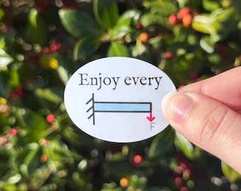 Puede incluir: Una pegatina ovalada con las palabras "Enjoy every" sobre un diagrama azul y negro con una flecha roja etiquetada "F". La pegatina se sostiene frente a un fondo de hojas verdes y bayas rojas.
