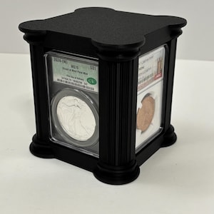 May include: Black display case with a square shape and fluted columns. The case holds two graded coins, one silver and one copper, visible through clear panels. The top of the case has a decorative design. Text on the coin holder reads "2024-(W) MS70 SS1".