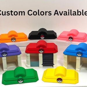 May include: A collection of 3D-printed Pokémon Center building models in various colors including orange, black, pink, purple, red, blue, green, and yellow. Each structure features a Poké Ball emblem on the roof. The text Custom Colors Available! is visible.