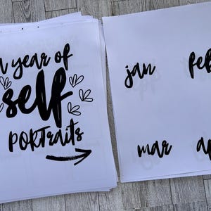 K&ouml;nnte beinhalten: Ein wei&szlig;es Blatt Papier mit schwarzem Text, der "a year of self portraits" lautet, mit einem schwarzen Pfeil, der nach rechts zeigt. Das Blatt ist in 12 Abschnitte unterteilt, die jeweils mit einem Monat des Jahres beschriftet sind: Jan, Feb, M&auml;r, Apr, Mai, Jun, Jul, Aug, Sep, Okt, Nov, Dez.