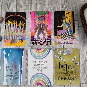 May include: A set of ten tarot cards with colorful illustrations and text. The cards include the following text: "There is a stream of love supporting my dreams", "The universe works fast when I'm having fun!", "Hope is the conduit for miracles", "King of Wands", "Justice", and "Ten of Swords".