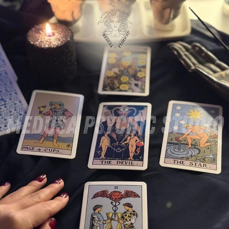 May include: A collection of tarot cards, including "Page of Cups," "The Devil," and "The Star," arranged on a dark surface. A lit black candle and a hand are also visible, suggesting a mystical or spiritual theme.