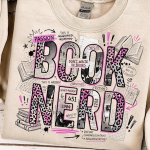 Può includere: Felpa beige con un design grafico che recita "BOOK NERD" in un mix di caratteri e accenti animalier. Il design include illustrazioni di libri, testi come "Passion", "Fiction" e gli anni 1984 e 2023.