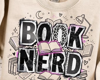 May include: A beige sweatshirt with the words "BOOK NERD" in a collage style design. The letters are decorated with patterns, including leopard print and newspaper clippings, with illustrations of books, a lamp, and stars.