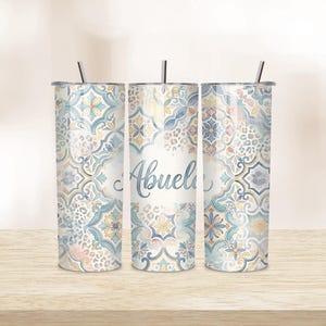 Può includere: Tre bicchieri in acciaio inossidabile con coperchi e cannucce. I bicchieri presentano un motivo ripetuto di disegni floreali e geometrici blu, gialli e bianchi. La parola "Abuela" è scritta in corsivo sul bicchiere centrale.