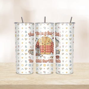 Peut inclure: Trois gobelets isothermes blancs avec des motifs floraux et en forme de cœur. Chaque gobelet porte l'inscription "Too Young for This, Too Old for TikTok" et un motif de cardigan, tasse à café et autres objets vintage.