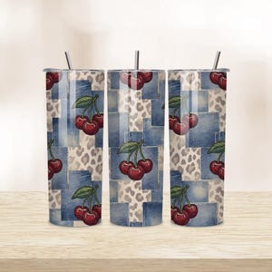 Puede incluir: Tres vasos de acero inoxidable con tapas y pajitas. Los vasos presentan un diseño de retazos de cuadrados de mezclilla, estampado de leopardo y cerezas. Las cerezas son rojas con hojas verdes. Los vasos están sobre una superficie de madera.