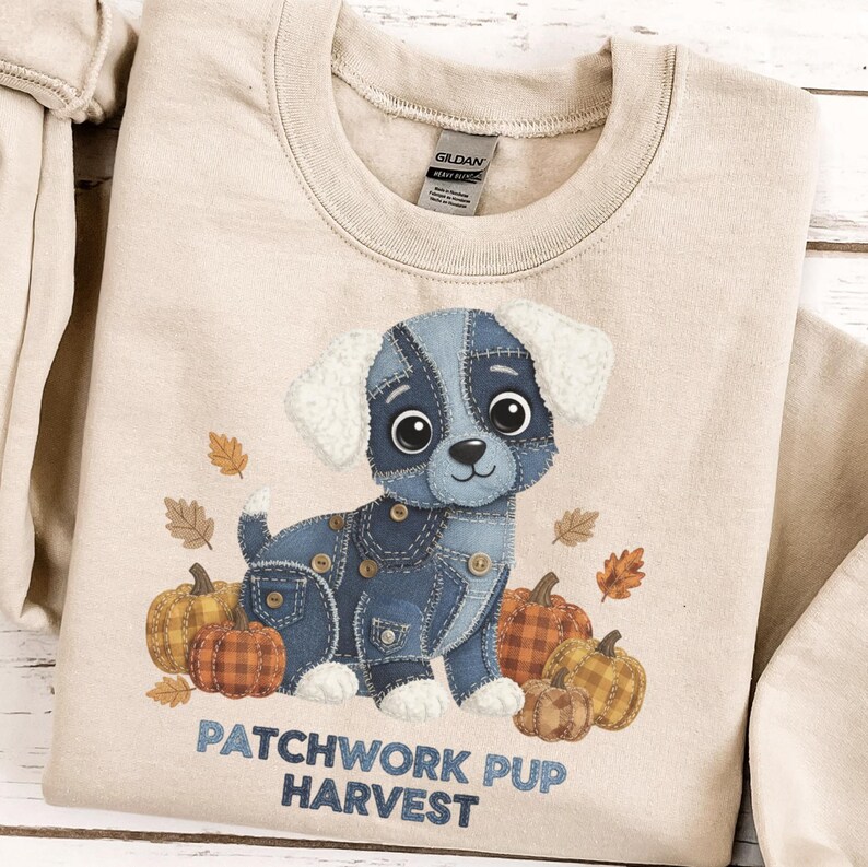 Puede incluir: Sudadera beige con un dise&ntilde;o de cachorro de retazos de mezclilla, rodeado de calabazas y hojas de oto&ntilde;o. El texto "PATCHWORK PUP HARVEST" est&aacute; impreso debajo. Cuello redondo, mangas largas.
